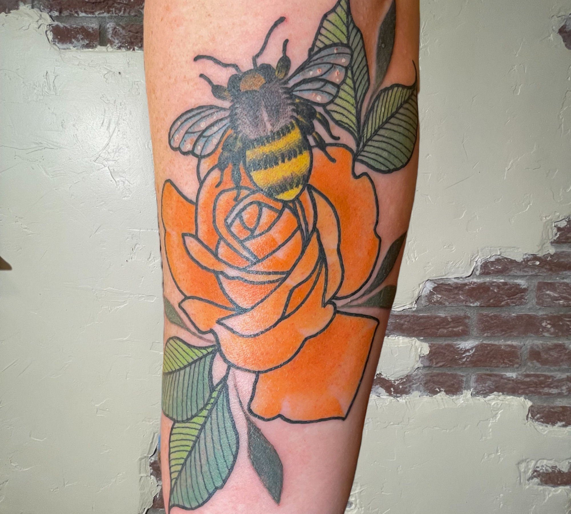 A tattoo of an orange rose and bee by Shannon Byrd of Fayetteville, AR