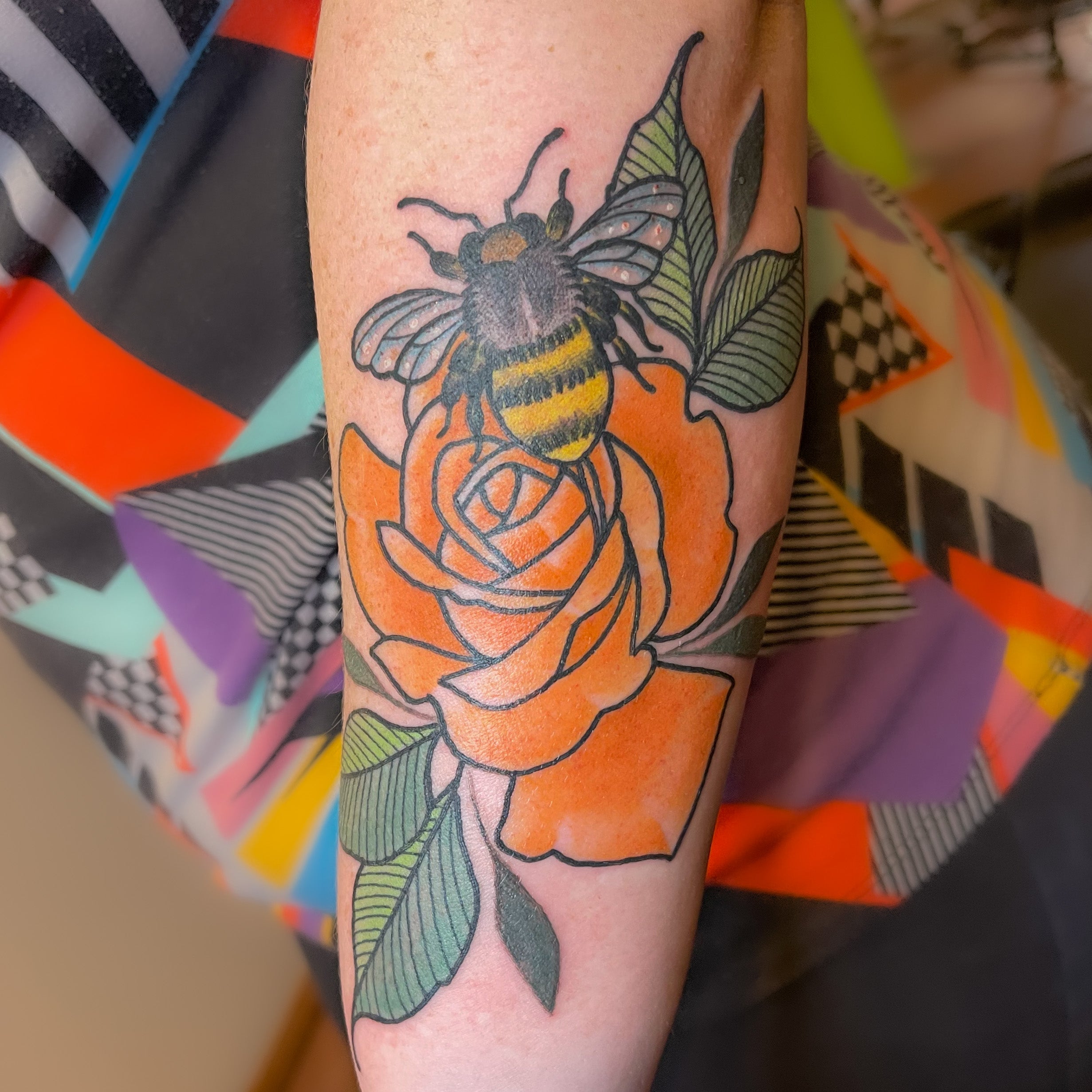 Tattoo of an orange rose with a bee by Shannon Byrd of Fayetteville