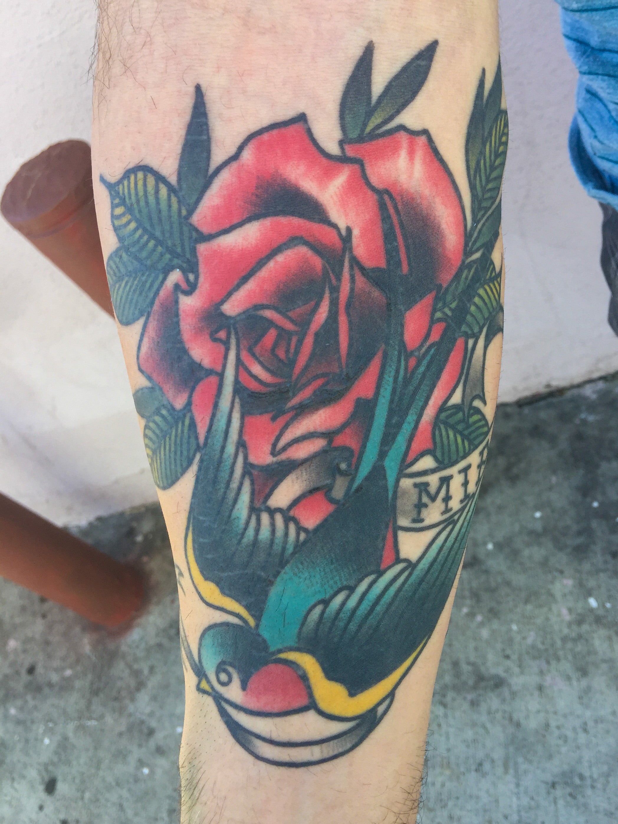 A tattoo of a rose and a colorful swallow in the traditional style by Shannon Byrd of Northwest Arkansas